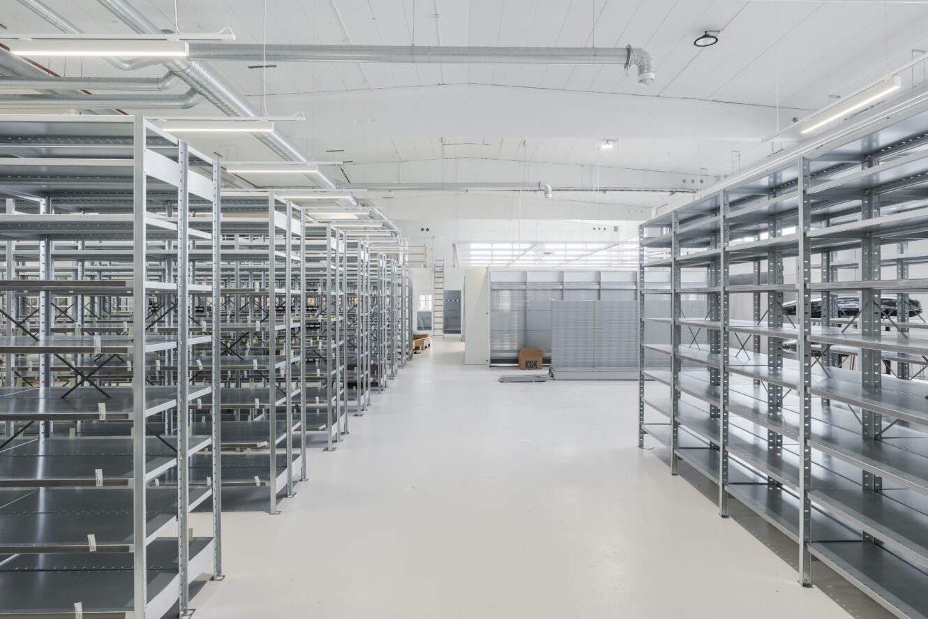 En rymlig, starkt upplyst lagerlokal med tomma metallhyllor i rader på ett rent vitt golv.