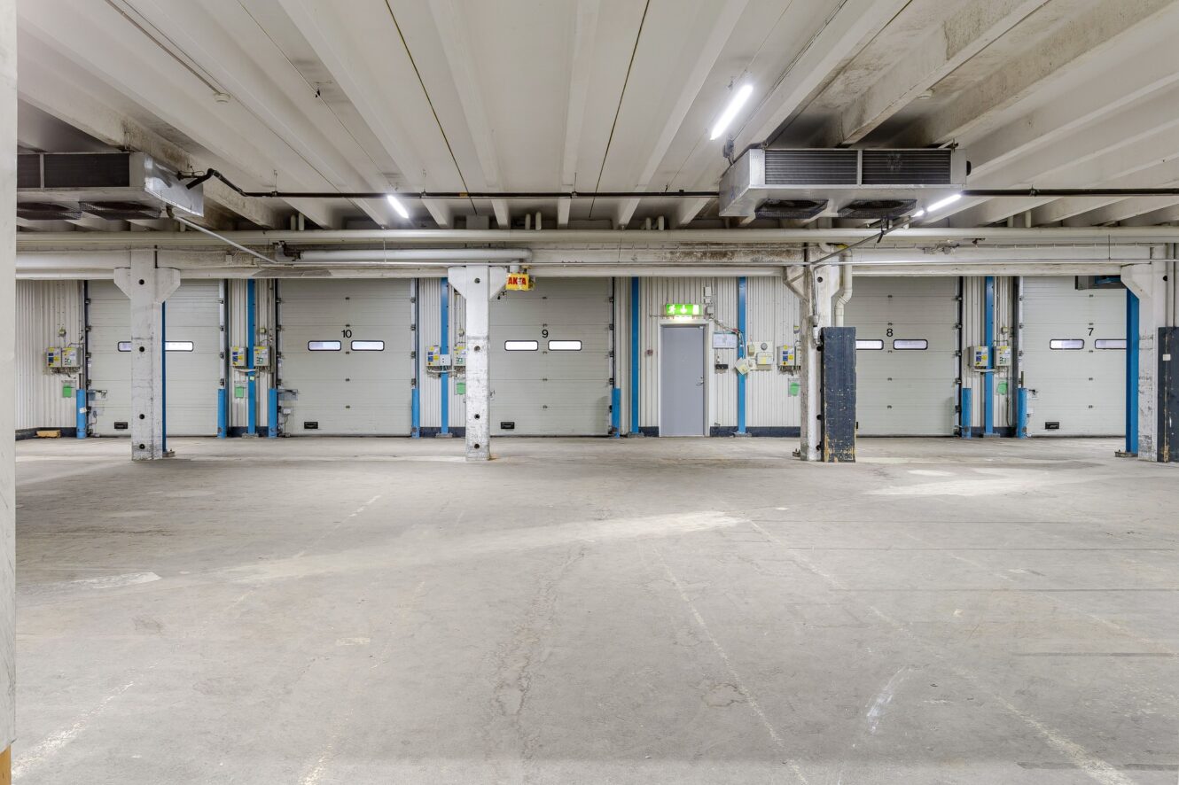 Ett stort tomt industriellt lagerutrymme med flera lastbryggor, betonggolv, vitt tak och takbelysning.