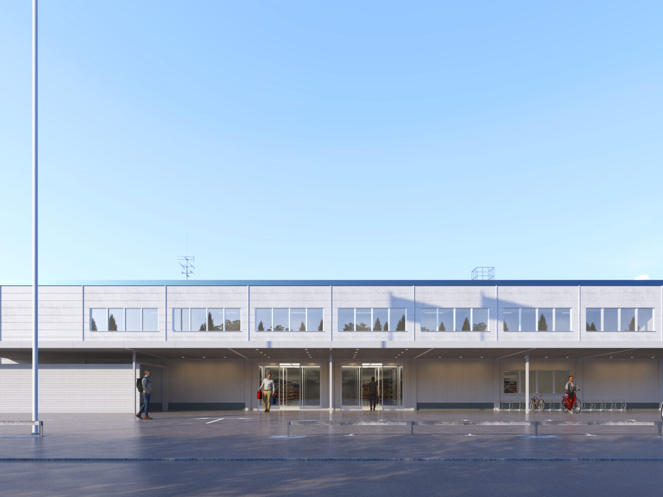 En modern tvåvåningsbyggnad med stora fönster och platt tak, med en glasad entré och en täckt gångväg, under en klarblå himmel.