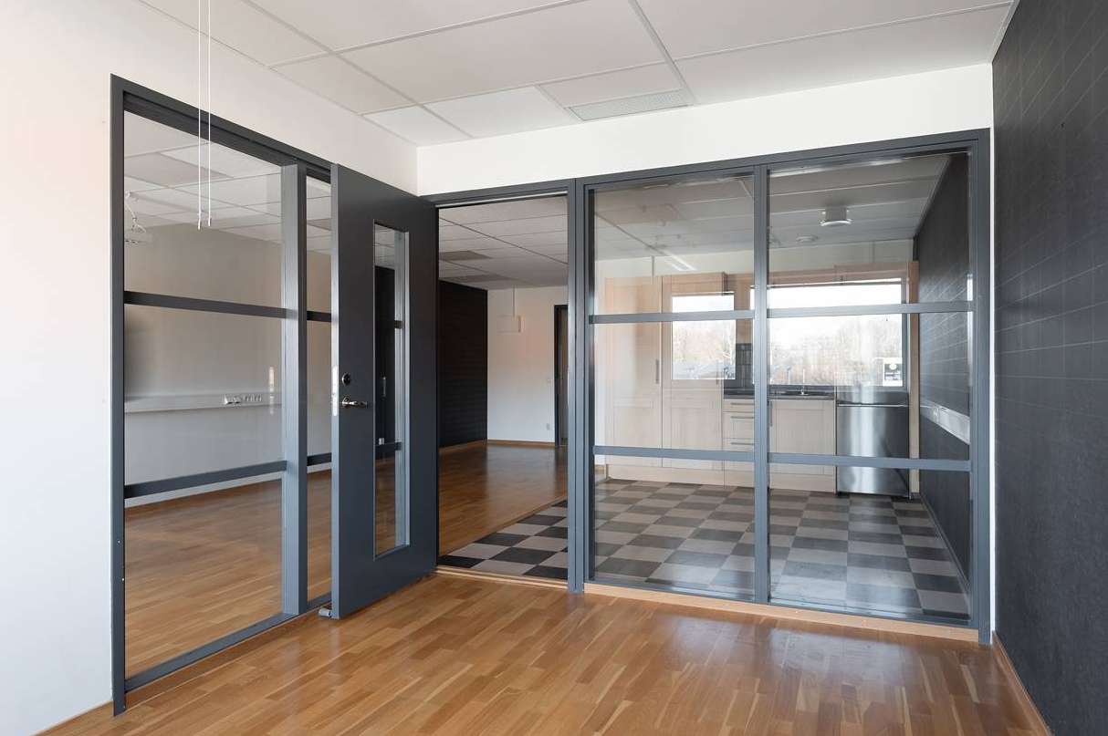 Moderna kontorslokaler med glasväggar, trägolv och ett pentry med svartvitrutigt kakel.