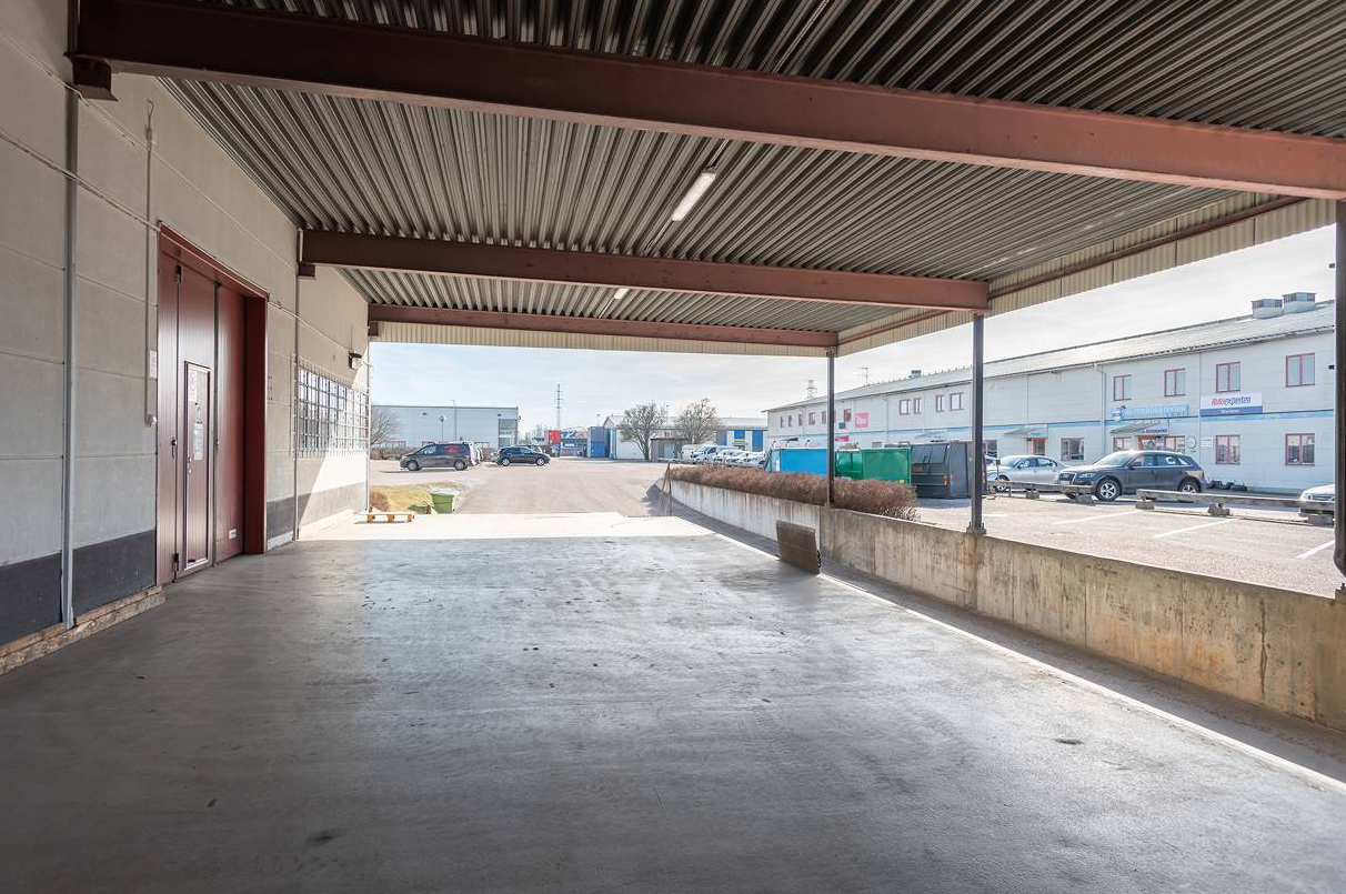 Överbyggd lastkaj med betongramp med utsikt över en parkeringsplats och industribyggnader under en klar dag.