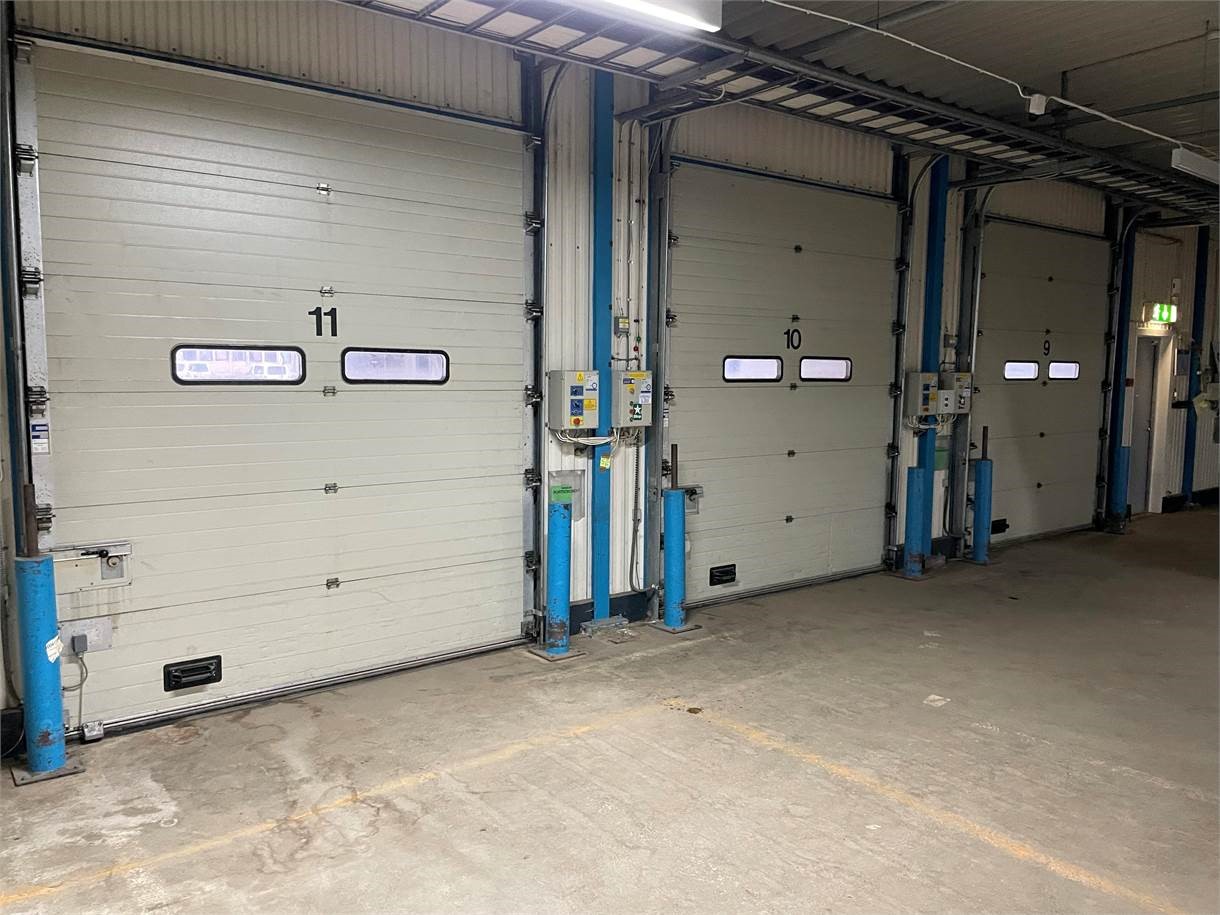 Tre industriella lastkajdörrar med nummer 9, 10 och 11 är stängda inne i ett stort lager. Kontrollpaneler och säkerhetspollare är placerade bredvid varje dörr.