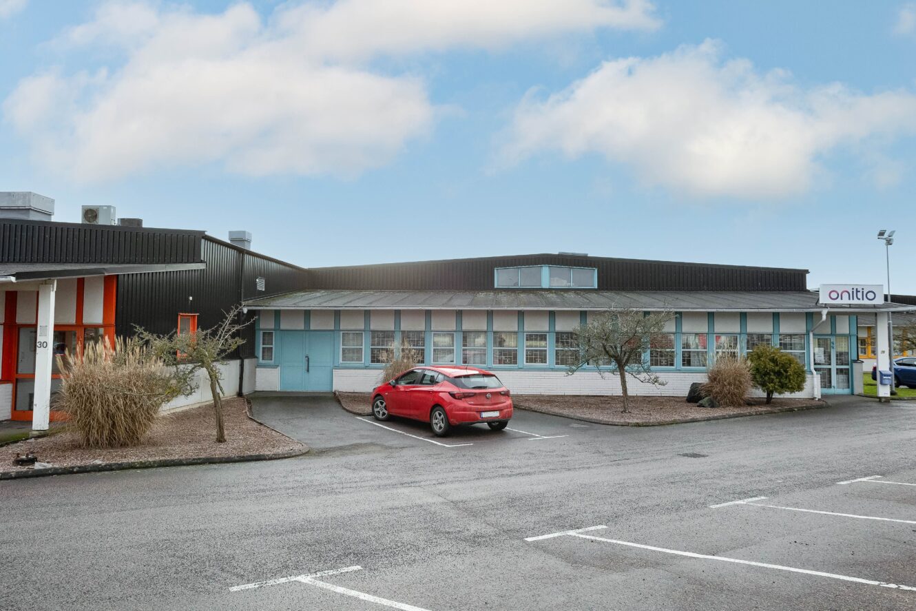 En röd bil står parkerad framför en envånings affärsbyggnad med en skylt som säger onitio under en delvis molnig himmel.