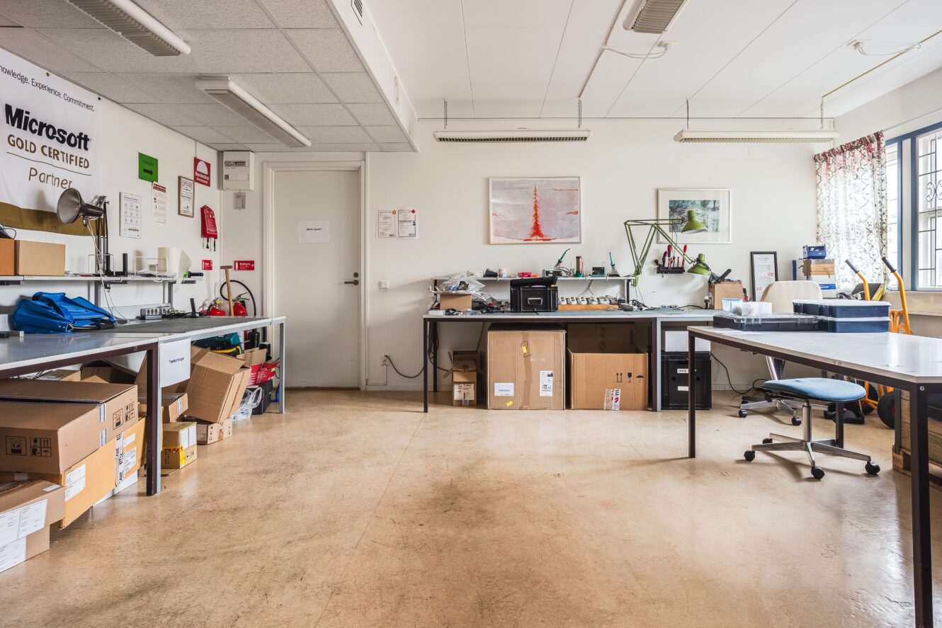 En prydlig kontorsarbetsplats med skrivbord, lådor, kontorsstolar, utrustning och väggdekorationer, inklusive certifikat och inramade bilder, i ett väl upplyst rum med fönster.