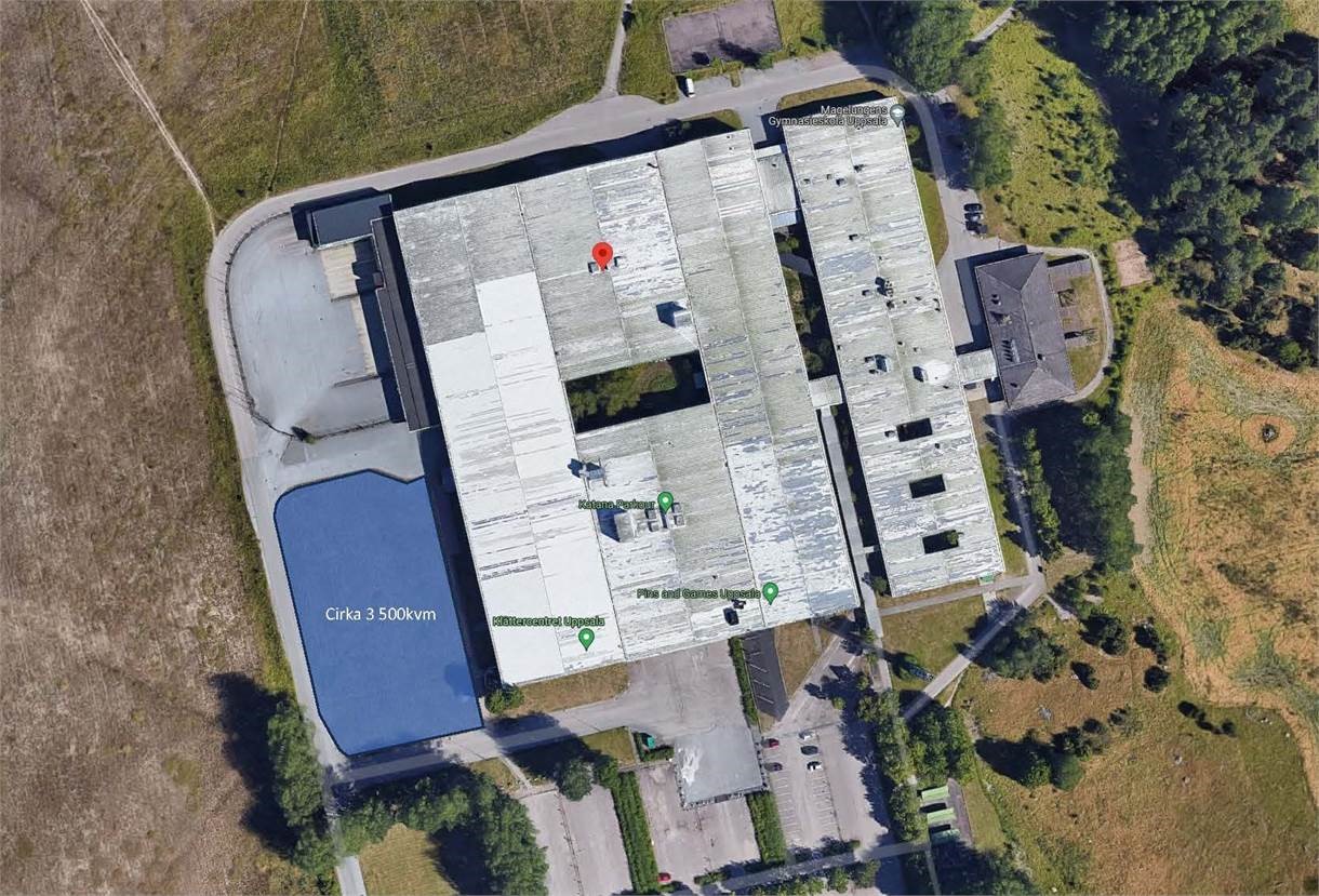 Flygfoto över en stor industribyggnad med vitt tak, intilliggande parkeringsplats, blåmarkerat utrymme märkt Circa 3500 kvm, och omgivande grönska.