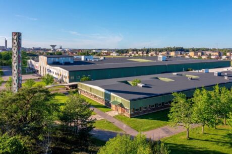 Flygfoto över en stor lagerbyggnad med ett högt, dekorativt torn i ett grönområde.