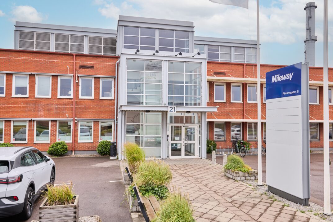 En modern kontorsbyggnad i tegel i två våningar med en ingång i glas, en vit skylt med texten Mileway och parkerade bilar framför.