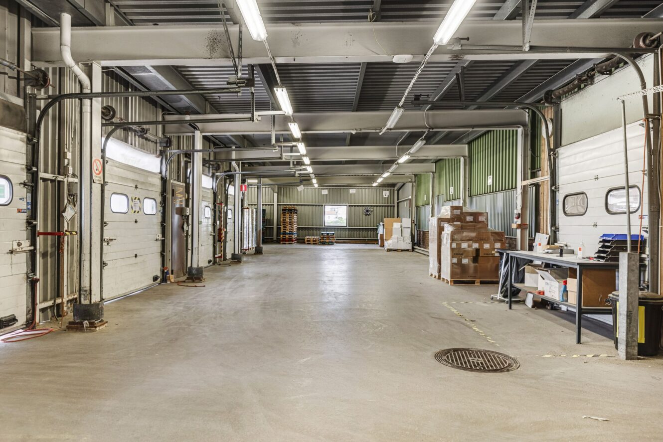 Industriell lagerlokal med flera garageportar, staplade kartonger, en arbetsstation med förnödenheter och lysrörsbelysning.