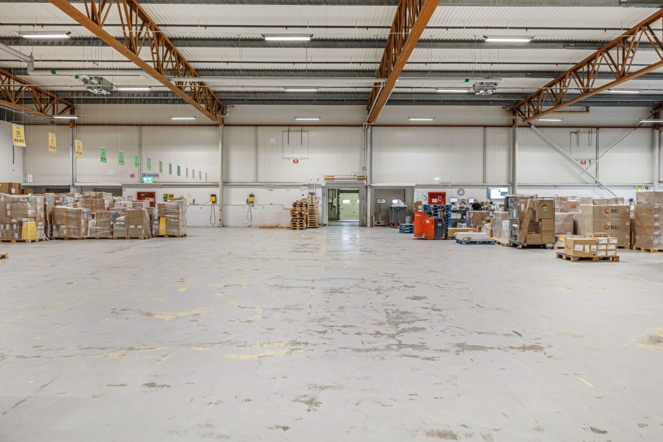 Rymlig lagerlokal med pallar, lådor och diverse utrustning längs väggarna; öppet golv i mitten.