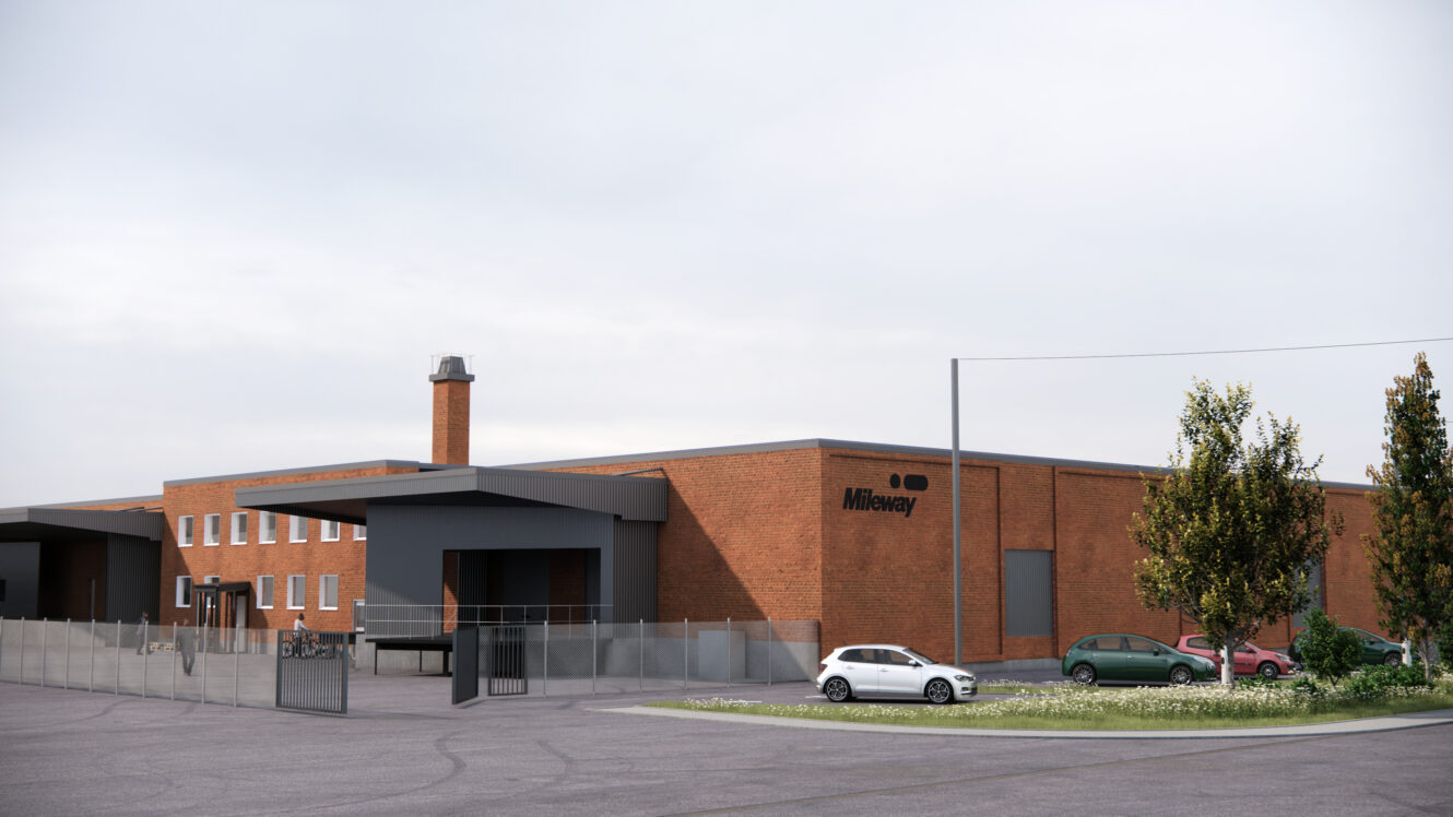 En stor industribyggnad i tegel med namnet Mileway omges av ett staket, parkerade bilar och några träd under en molnig himmel.