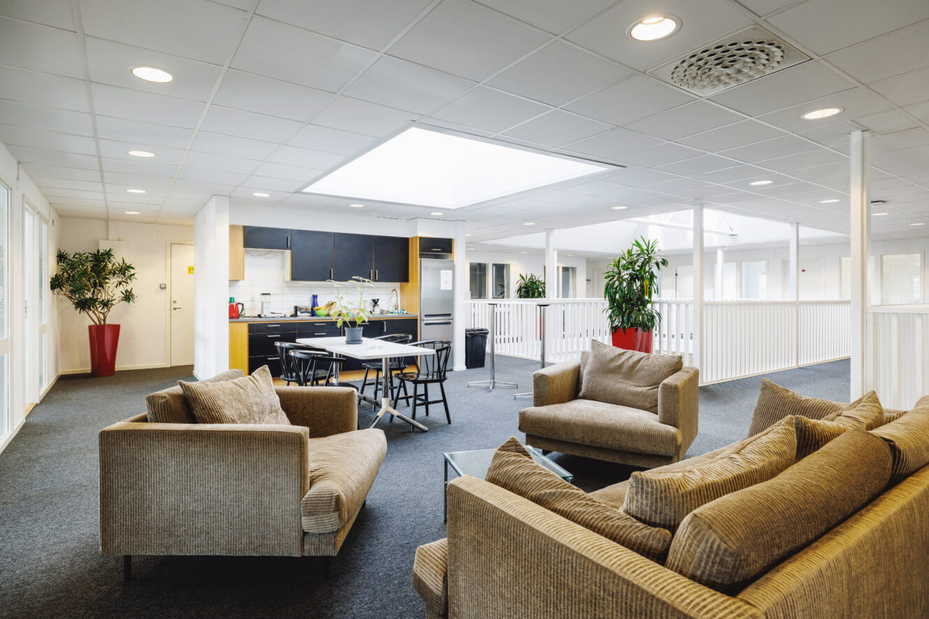 Ett modernt vardagsrum och kök i öppen planlösning med beige soffor, ett runt matbord, svarta stolar och krukväxter.