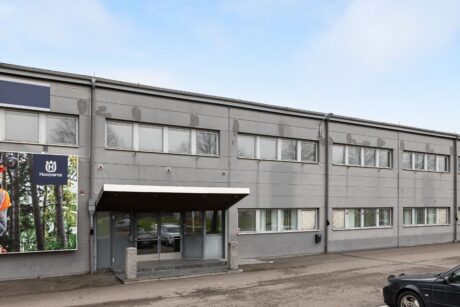 En grå affärsbyggnad i två våningar med stora fönster och en täckt entré, med en Husqvarna-reklam på vänster sida.