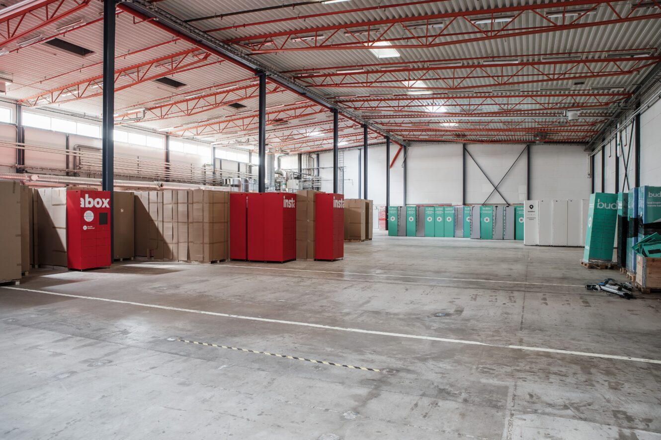 Rymlig lagerlokal med röda och gröna förvaringsskåp, stora staplar med kartonger och synliga takbjälkar.