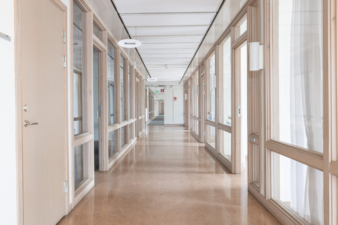 En ren, tom korridor i en kontorsbyggnad eller på en vårdinrättning med glasdörrar och skyltar som hänger från taket.