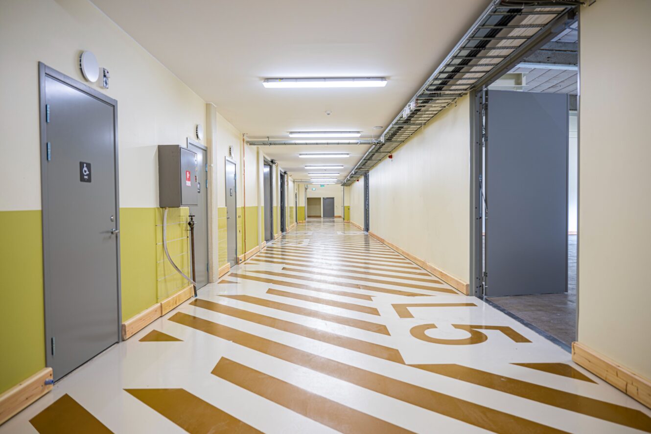 Bred korridor i en modern byggnad med dörrar på båda sidor, takbelysning, elskåp och stor C5-markering på golvet.