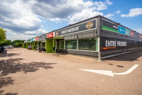En motorcykelhandlarbyggnad med Harley-Davidson och andra varumärkesskyltar, en stor ENTRÉ PROBIKE-skylt, motorcyklar parkerade utanför och en delvis molnig himmel ovanför.