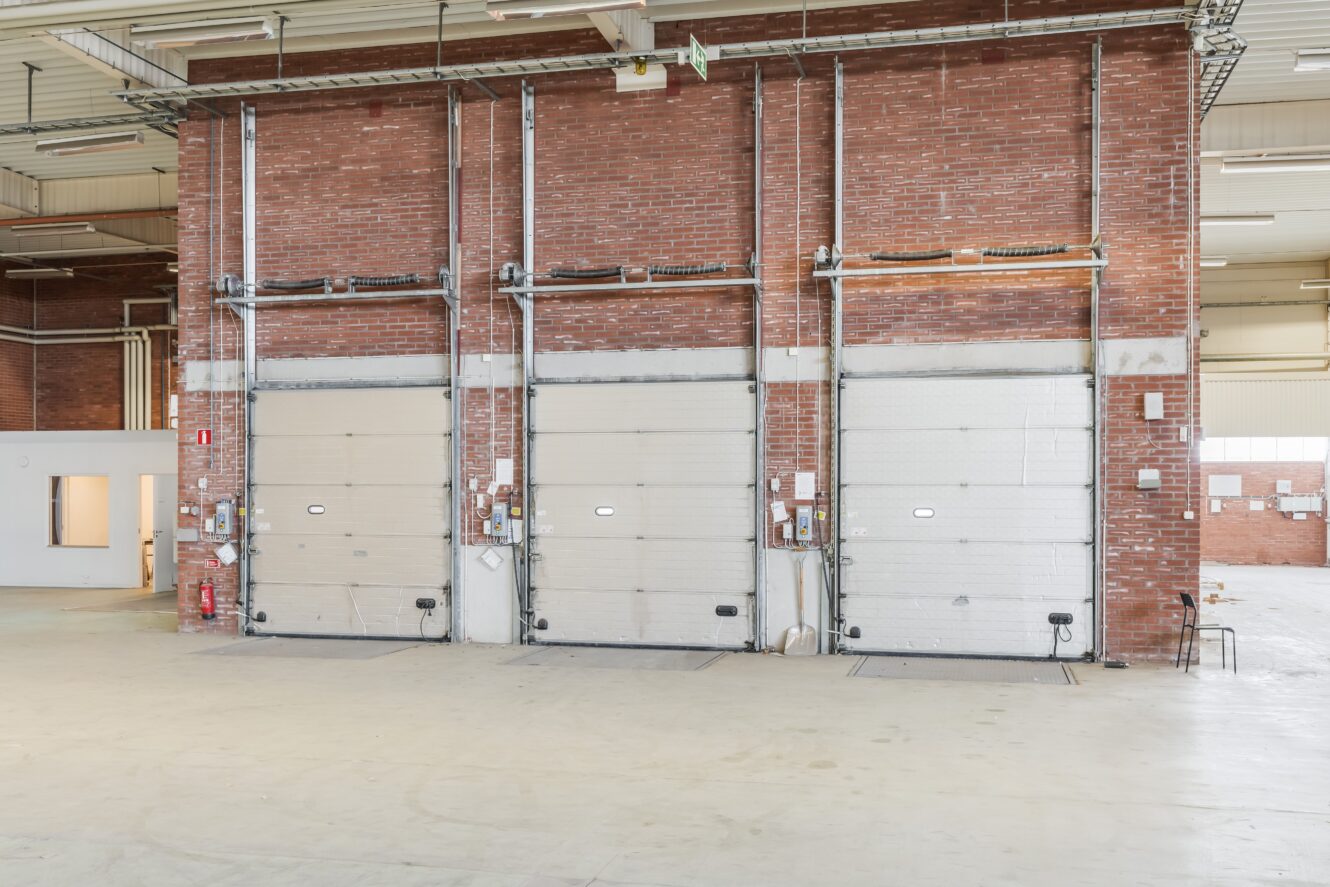 Tre stängda industriella garageportar i en tegelvägg inne i en rymlig, tom lagerlokal.