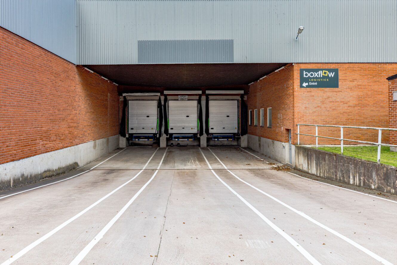 Tre lastkajer med stängda dörrar i en lagerlokal; på en skylt på väggen står det boxflow logistics.