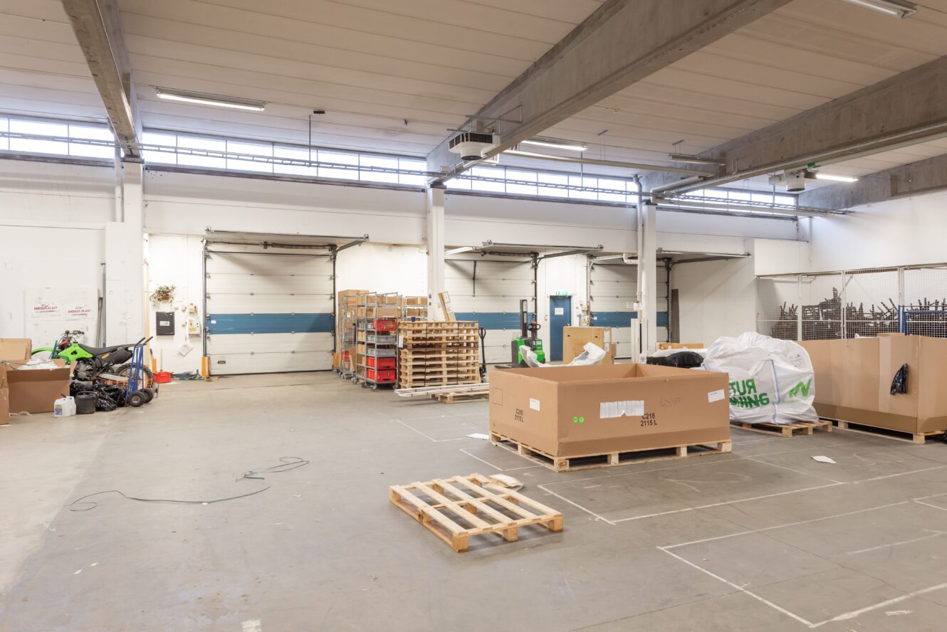 En lagerlokal med pallar, kartonger och diverse utrustning utspridda på golvet nära lastbryggor.