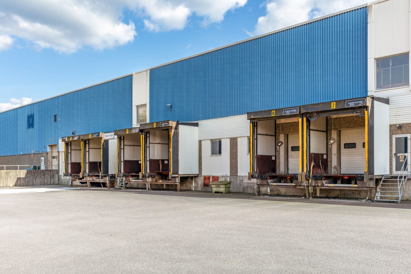 Lastkajer med fyra lastbilsuppställningsplatser vid en lagerbyggnad, med stängda lastkajdörrar och en i stort sett tom asfalterad yta framför.