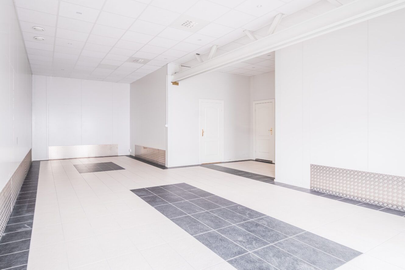 Tomt, rent och modernt rum med klinkergolv, vita väggar, två stängda vita dörrar och takbelysning.