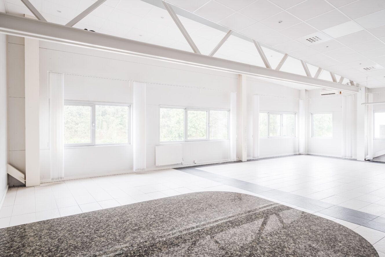 Ett stort, tomt och ljust rum med vita väggar, klinkergolv och flera fönster som släpper in naturligt ljus.