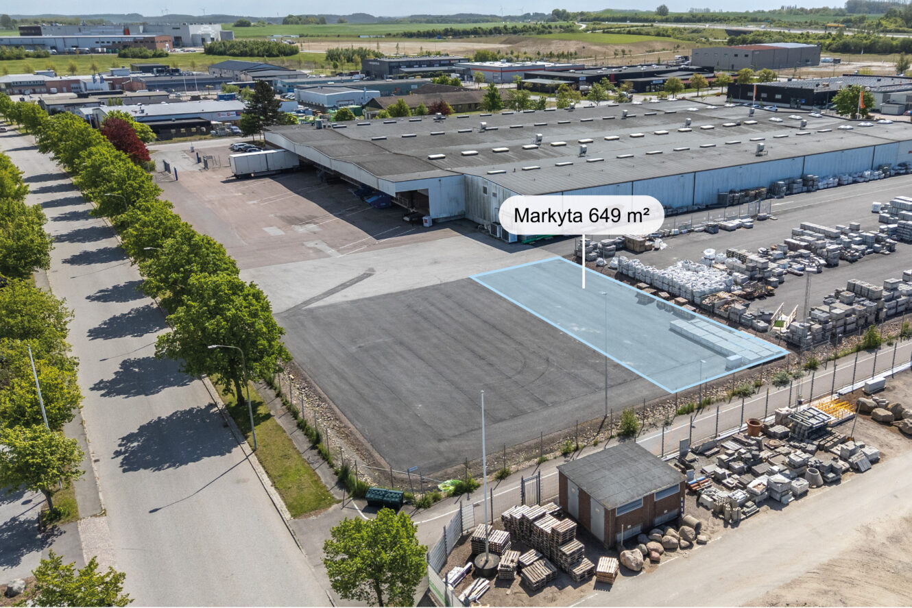 Flygfoto över en industrianläggning med en yta på 649 m², märkt ”Markyta”, på en asfalterad tomt intill en byggnad och lagrat material.