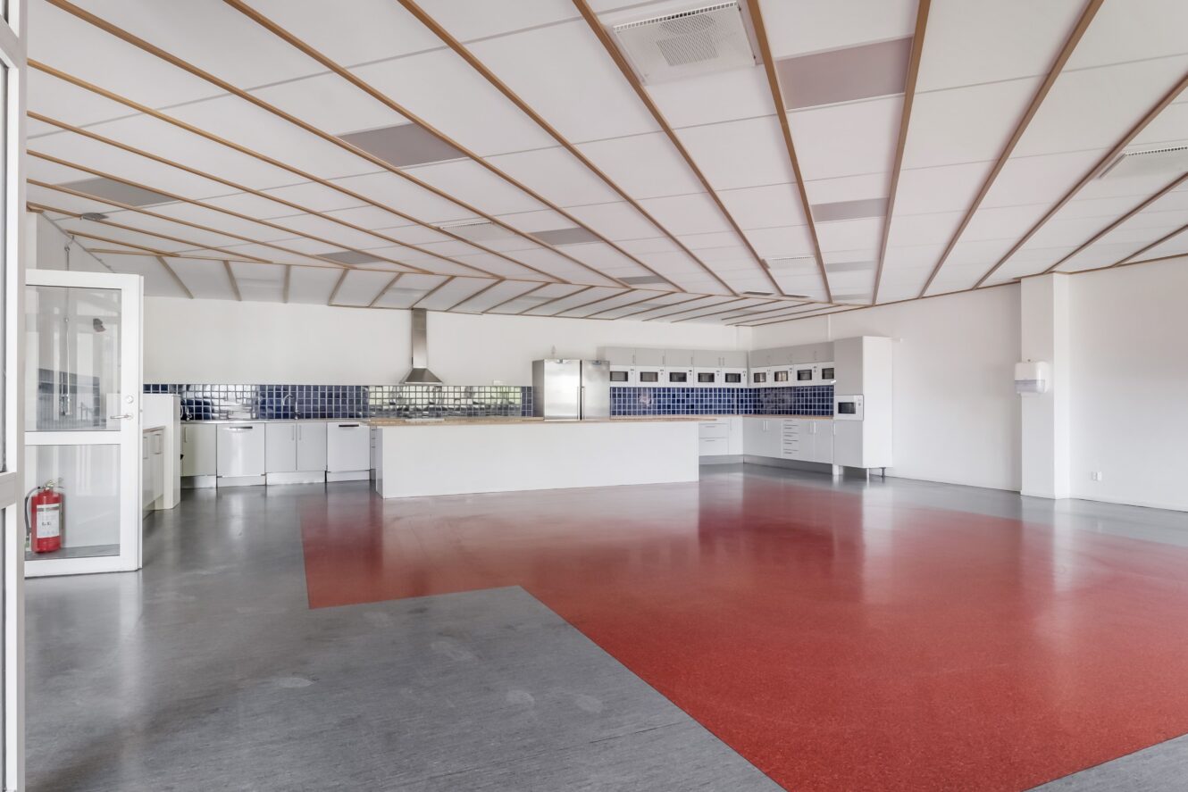 Rymligt, modernt kök med rött och grått golv, vita skåp, blå kakelplattor och vitvaror i rostfritt stål i ett ljust, öppet rum.