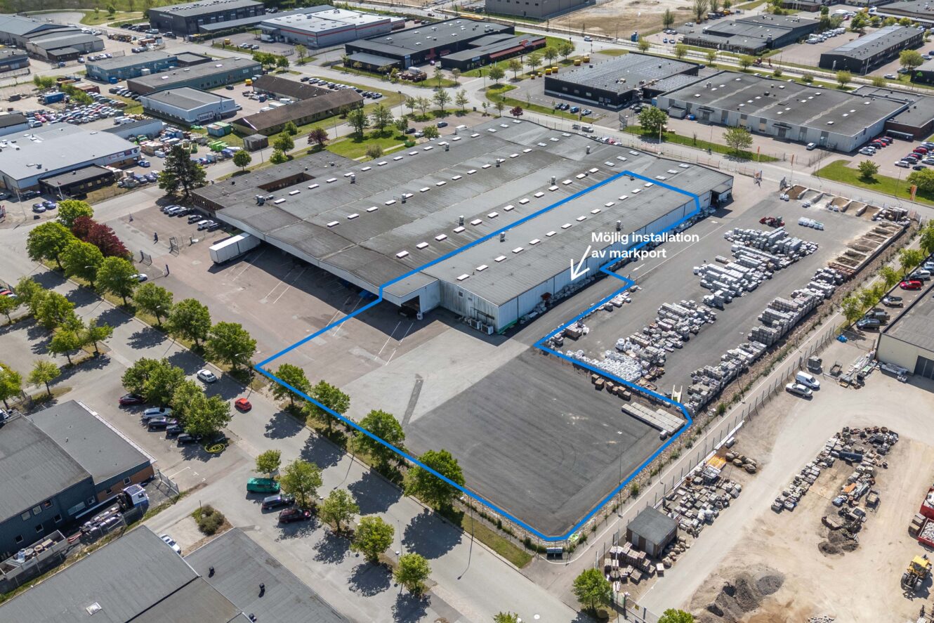 Flygfoto över en industribyggnad med parkeringsplatser och omgivande lagerlokaler; en del är markerad i blått med text som indikerar en möjlig installation av en ny lastport.