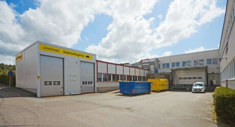 Industriellt lastkajsområde med två stora rullportar, en liten vit skåpbil, blågula containrar och en byggskylt med Godsmottagning.