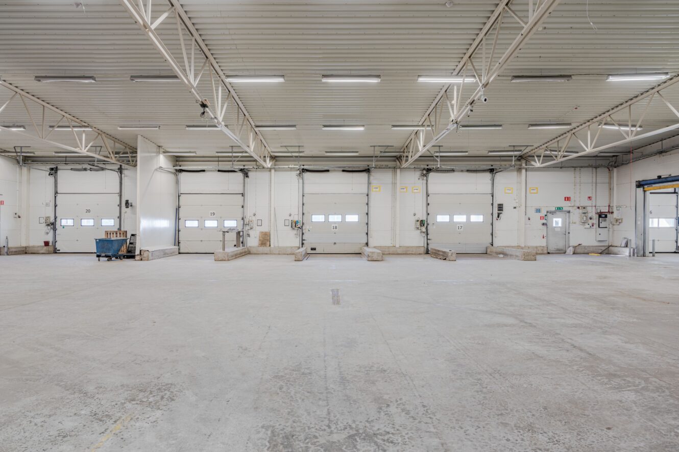 Rymlig, tom industrilagerlokal med flera lastbryggor, betonggolv och takbelysning.