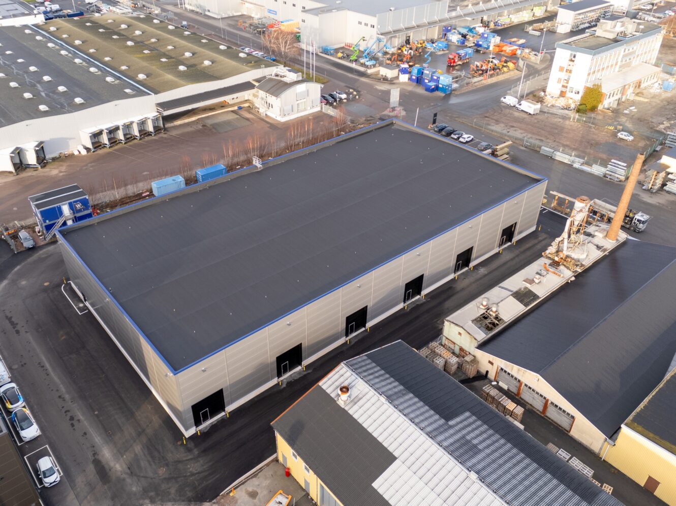Flygfoto över ett stort industrilager med flera lastkajer, omgivet av andra kommersiella byggnader och fordon.