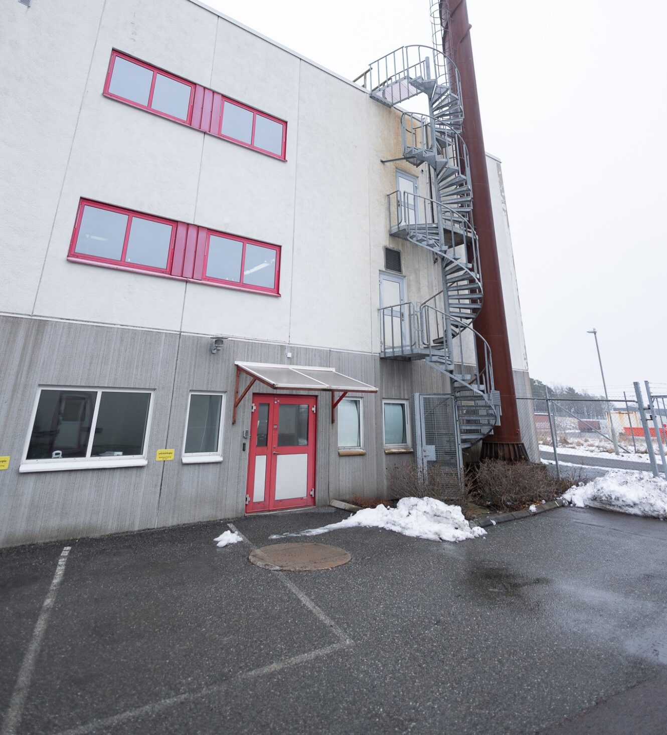 En trevåningsbyggnad med rödfärgade fönster och dörrar, en utvändig spiraltrappa och snöfläckar på marken.