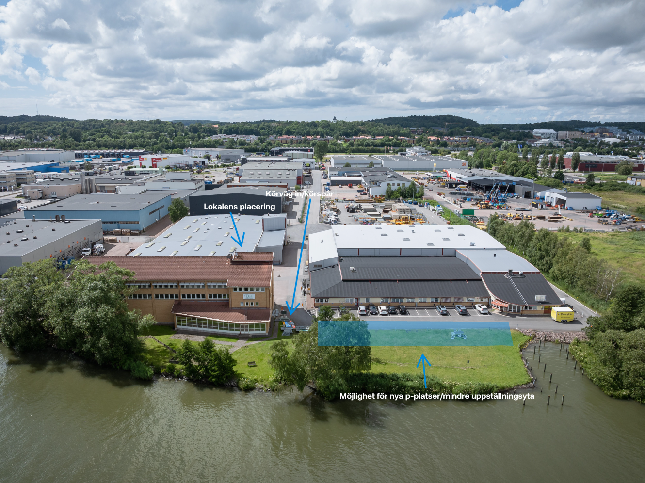 Flygfoto över ett industriområde vid en flod med flera lagerbyggnader. Blå pilar och etiketter visar var byggnaderna ligger och var det finns plats för nya parkeringsplatser eller lagerutrymmen.