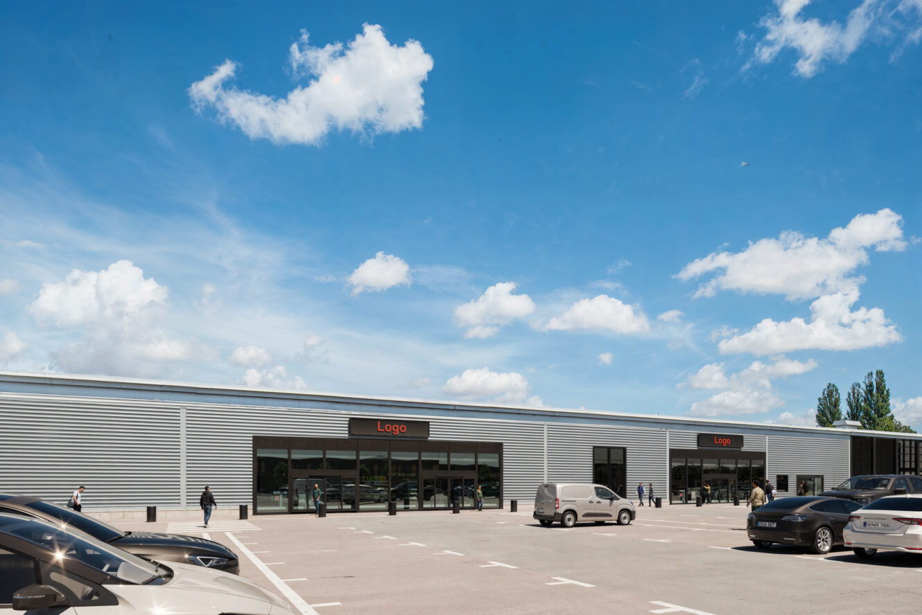 En modern affärsbyggnad med en stor parkeringsplats framför, flera parkerade bilar, människor som promenerar och en blå himmel med spridda moln ovanför.