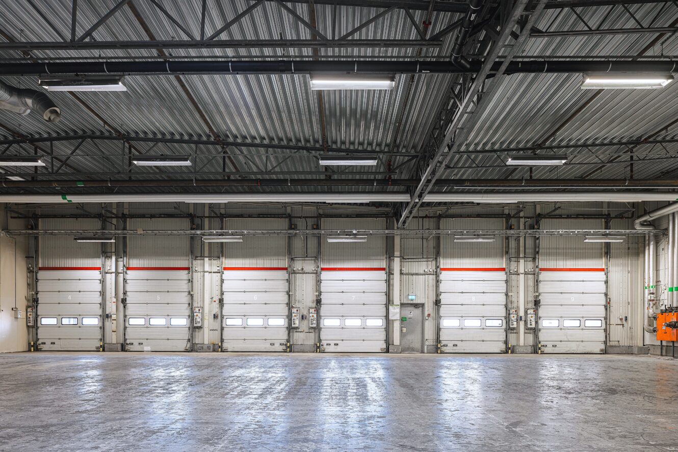 Invändig vy av ett tomt industrilager med ett polerat betonggolv och fem stora lastkajsdörrar.