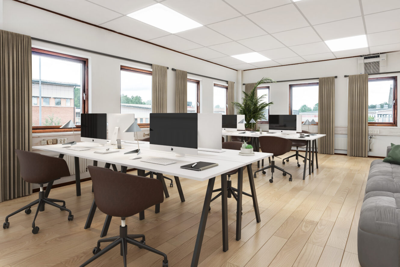 Modernt kontor med flera skrivbord, datorer, snurrstolar, stora fönster, ljust trägolv och inredning i neutrala färger. En krukväxt står nära mitten av rummet.