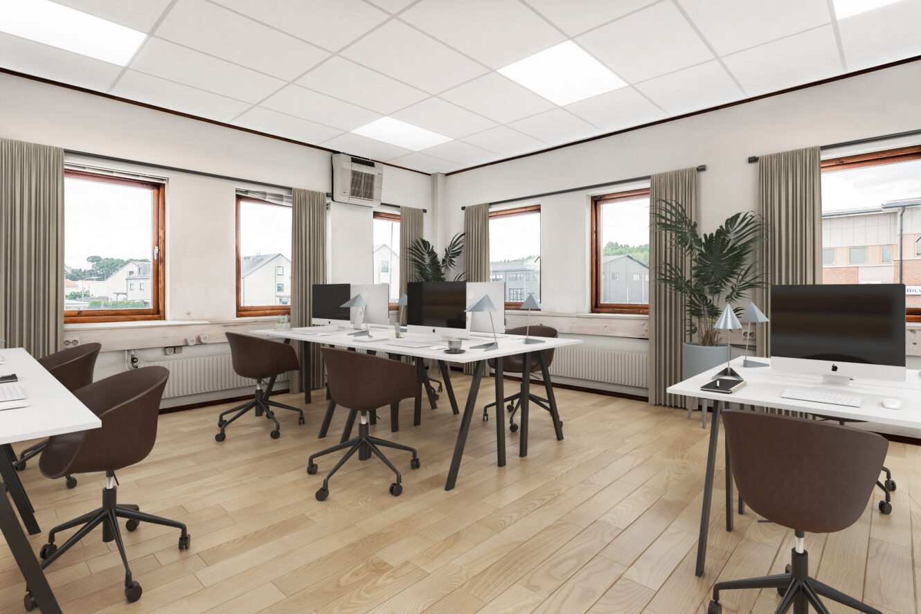 Modernt kontor med trägolv, flera skrivbord och stolar, stationära datorer, stora fönster med gardiner och två krukväxter.