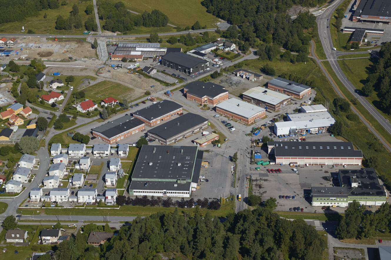 Flygbild över ett industri- och bostadsområde med lagerlokaler, kontorsbyggnader, hus, vägar och omgivande grönska.