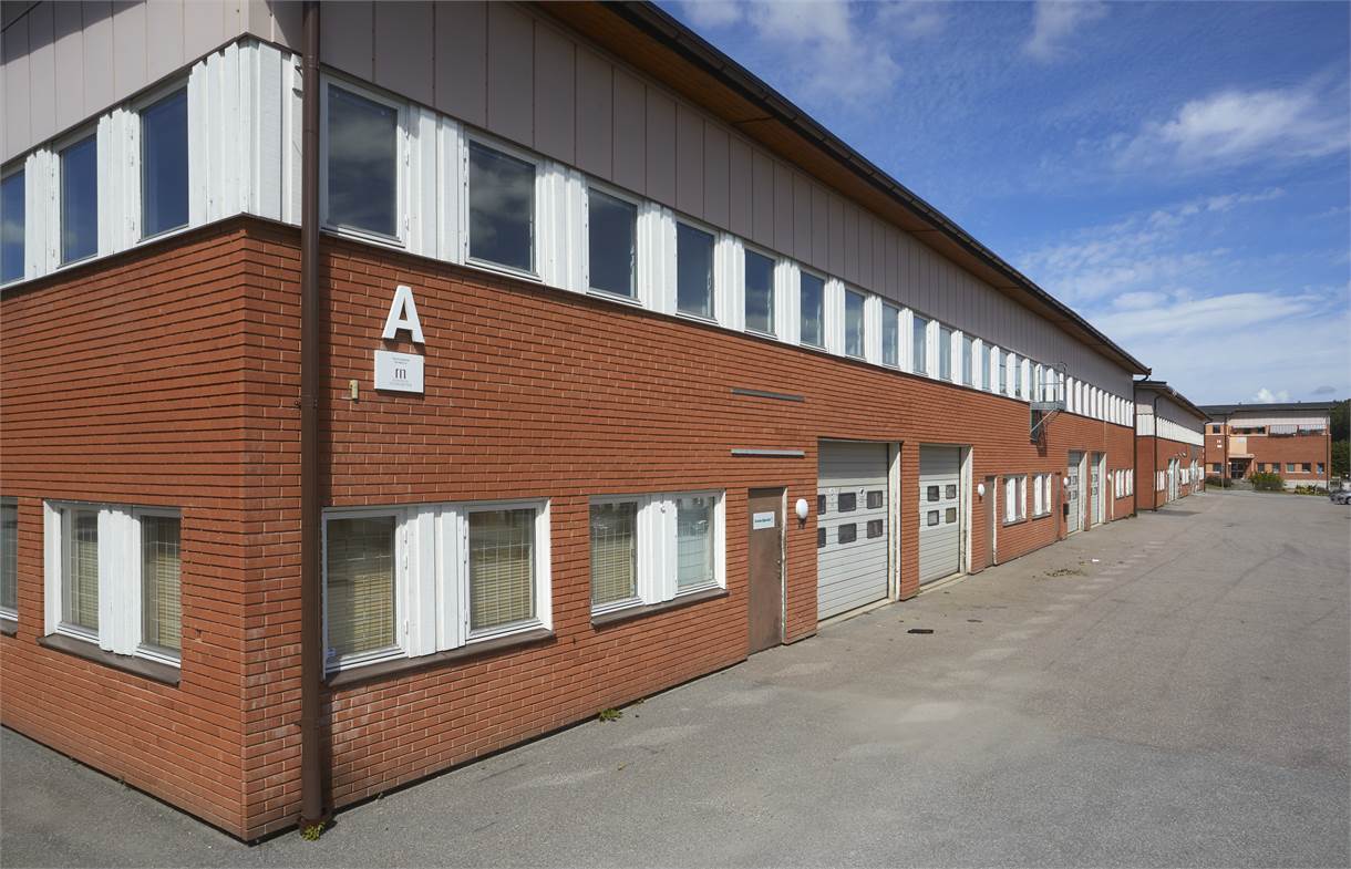 En stor industribyggnad i tegel med vitkarmade fönster och garageportar, märkt med bokstaven A, en klar dag.