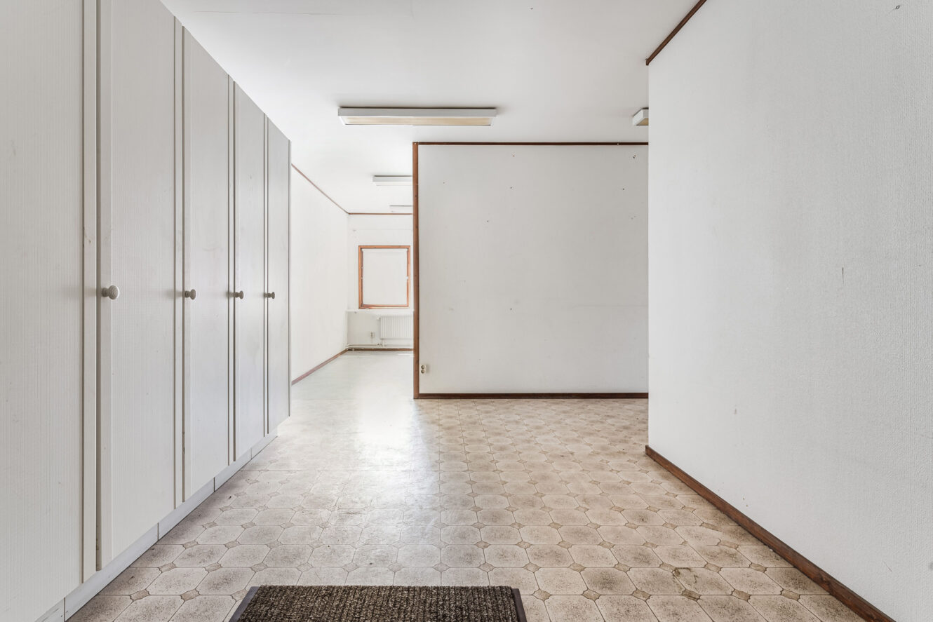 Ett ledigt, omöblerat rum med vita väggar, inbyggda vita garderober till vänster, klinkergolv och ett fönster längst bort.