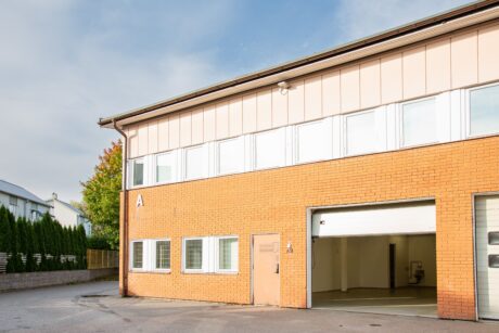 En kommersiell byggnad i två våningar med gult tegel på nedre plan, beige övre paneler och en stor garageport som är delvis öppen.