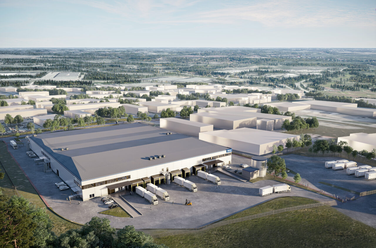 Flygfoto över en stor lagerlokal med flera lastkajer och lastbilar parkerade utanför, omgiven av industribyggnader och grönska.