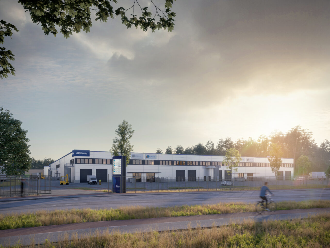 En stor industribyggnad med Miltenyi-skyltar, omgiven av stängsel och träd, syns i soluppgången. En cyklist cyklar längs vägen i förgrunden.