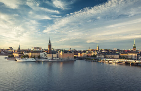 En panoramautsikt över Stockholms hamn med historiska byggnader, kyrktorn och ett fartyg i hamn under en delvis molnig himmel.