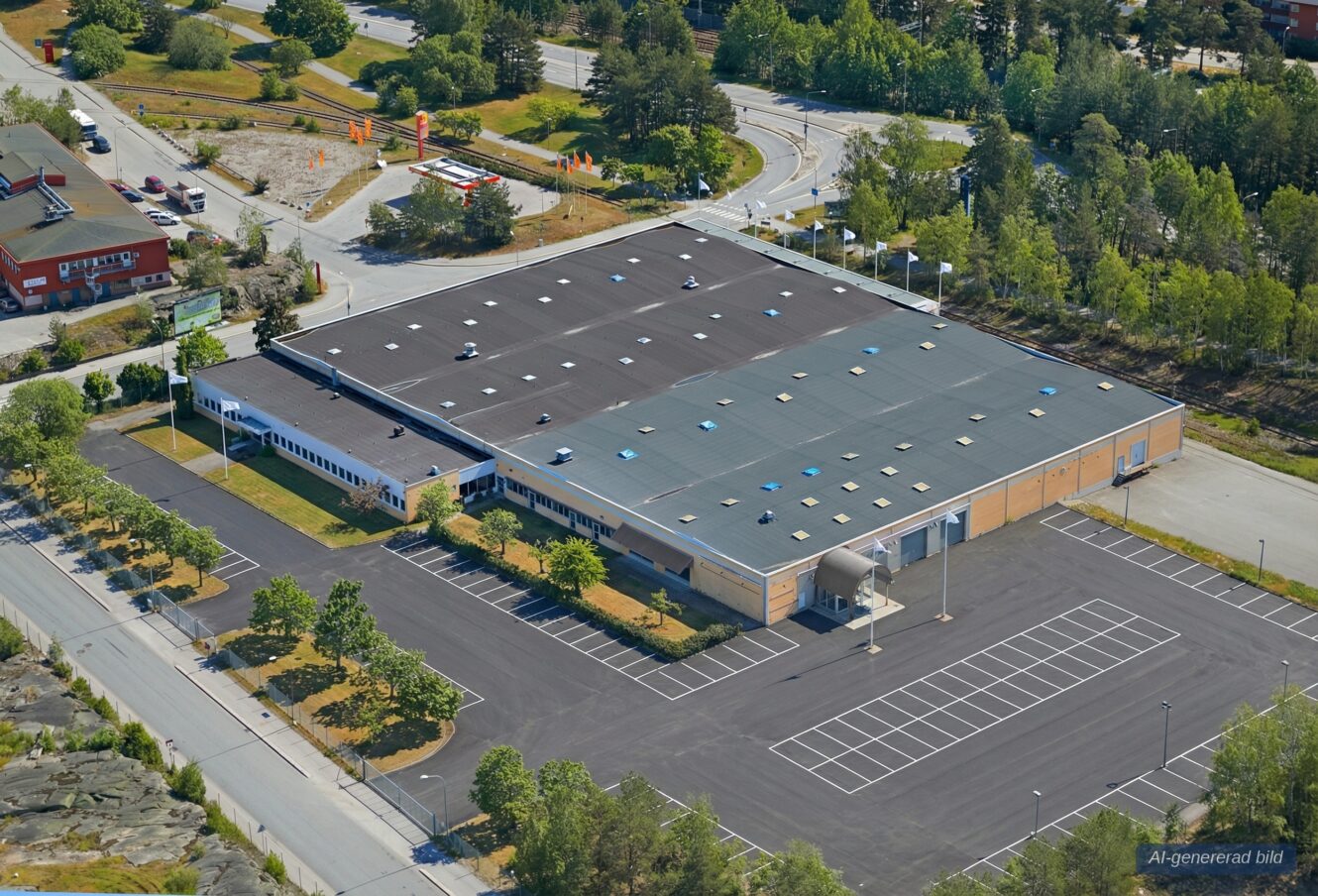 En stor affärsbyggnad med en våning och en i stort sett tom parkeringsplats, omgiven av träd och vägar, sedd från ovan.