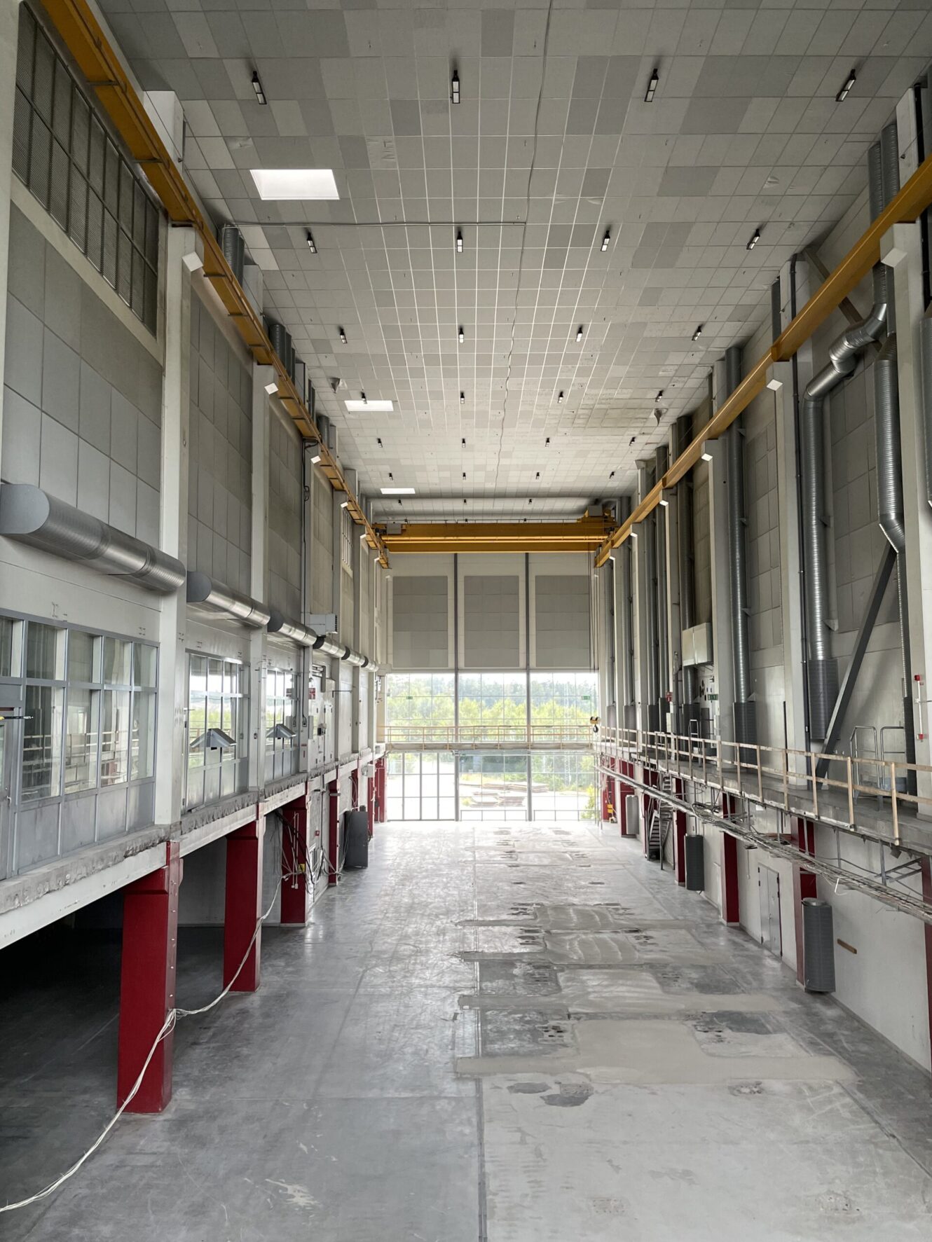 En rymlig, tom industrilokal med högt i tak, stora fönster längst in, lyftkranar och diverse rör och plattformar längs väggarna.