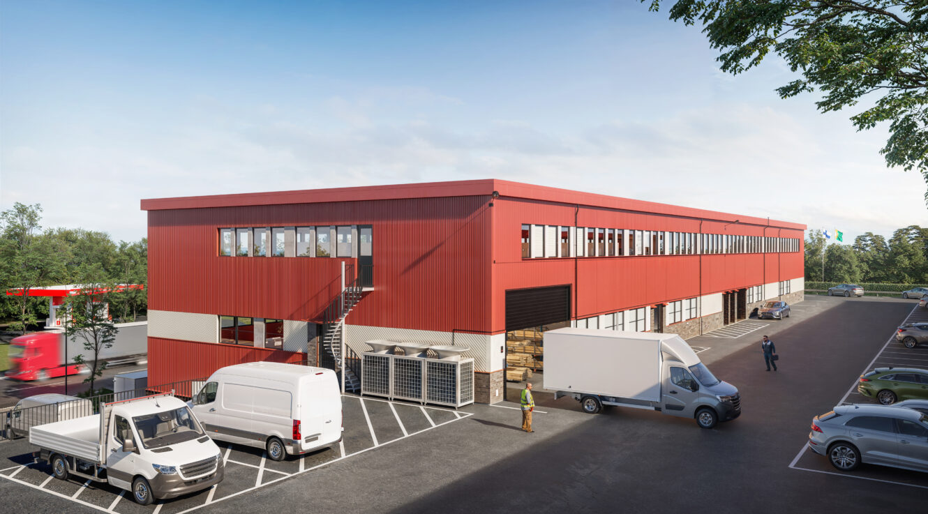 En stor röd industrihall med flera lastbilar parkerade utanför, en som lastar vid en brygga och bilar på en parkeringsplats i närheten en klar dag.