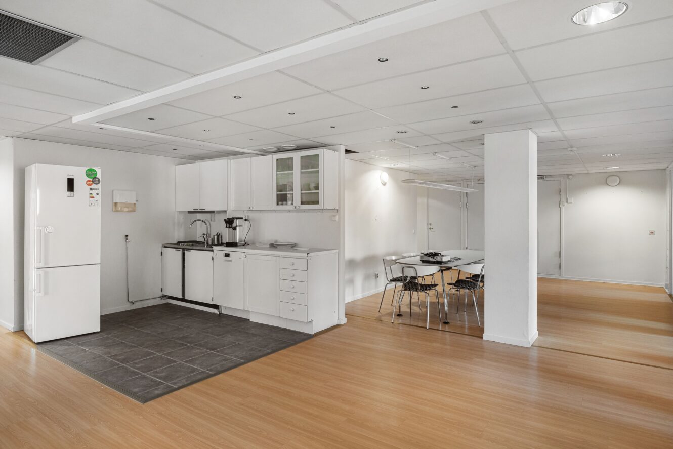 Ett modernt, minimalistiskt kök med vita skåp, kylskåp och en matplats med bord och stolar på ett ljust trägolv.