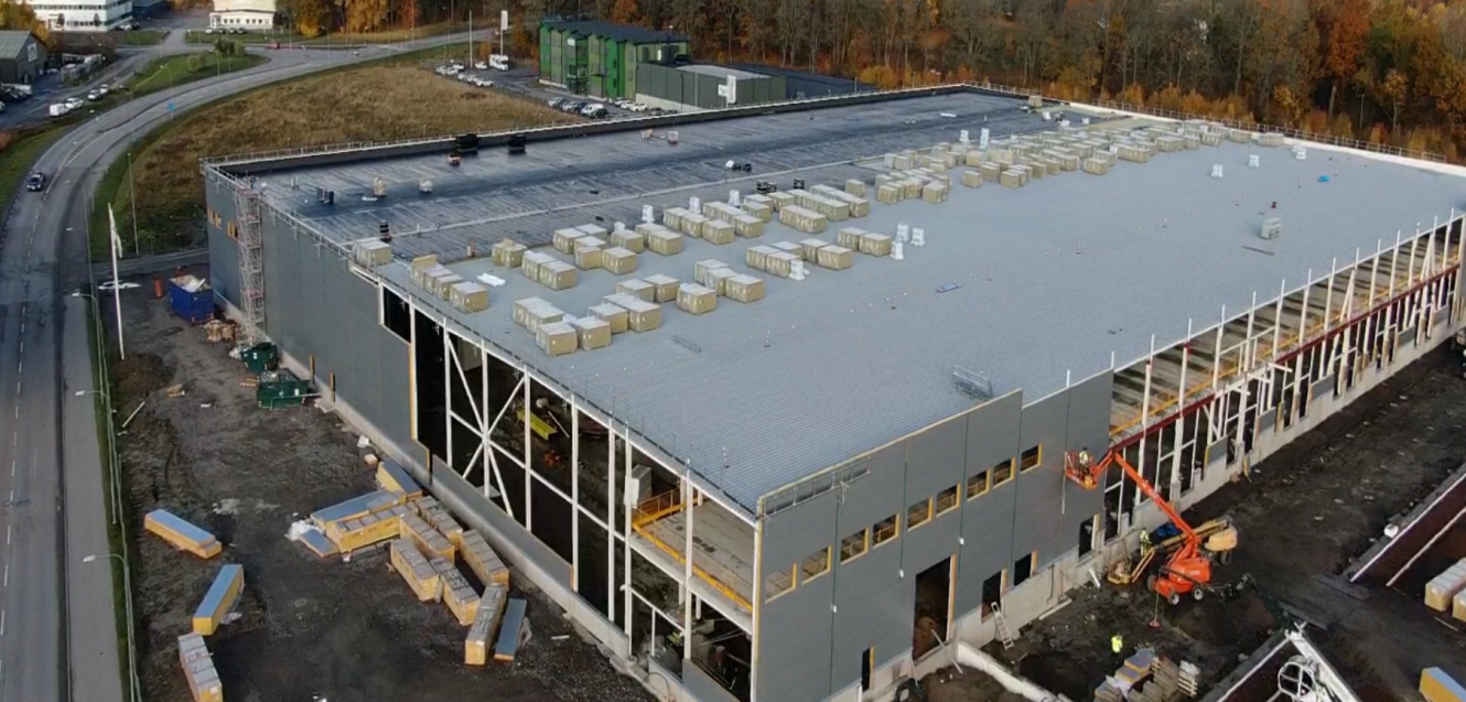 En stor industribyggnad under uppförande med material och byggutrustning utspridda på platsen.